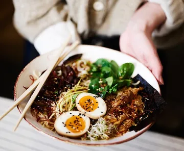 Person hält Schüssel Ramen mit Essstäbchen.