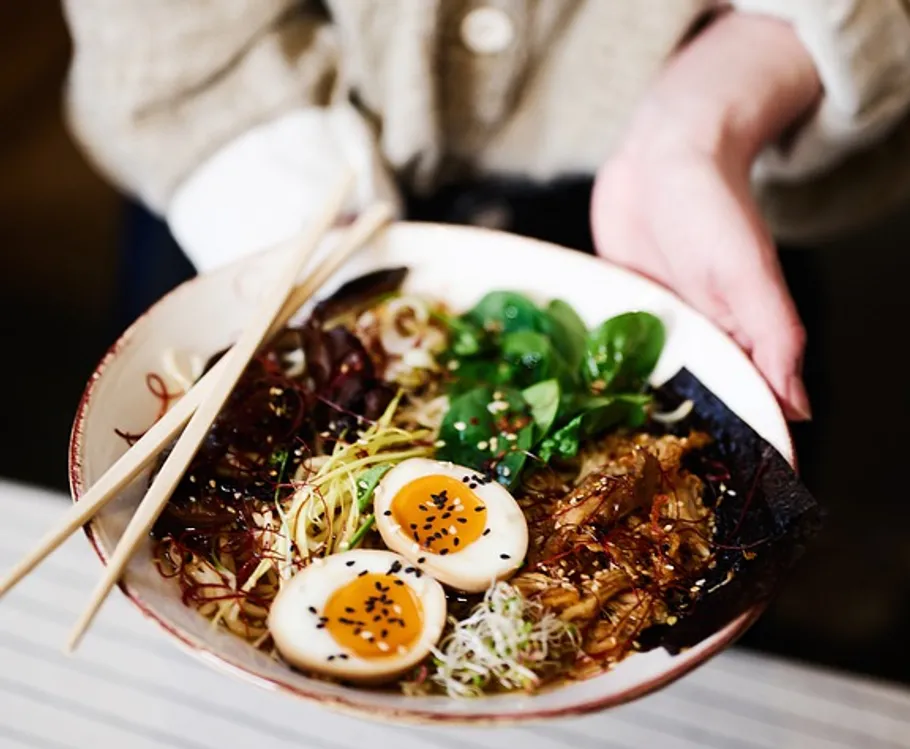 Person hält Schüssel Ramen mit Essstäbchen.