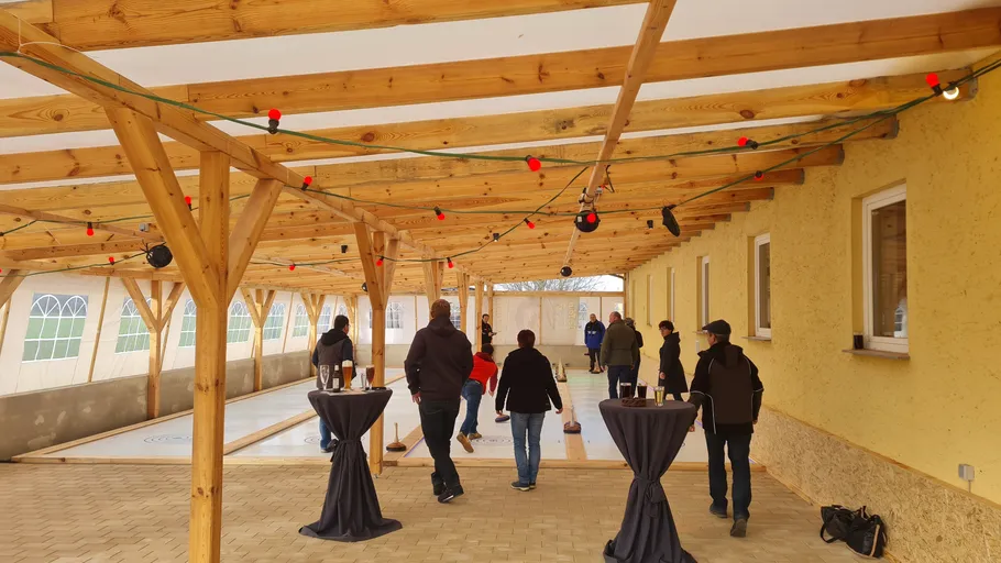 Leute spielen Eisstockschießen unter Holzpergola.