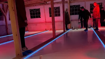 People playing curling indoors on ice rink.