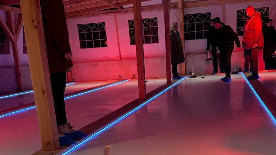 Personen spielen Curling auf Eisbahn drinnen.