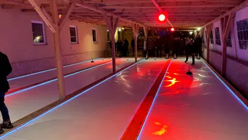 Überdachte Eisbahn mit Menschen beim Spiel.