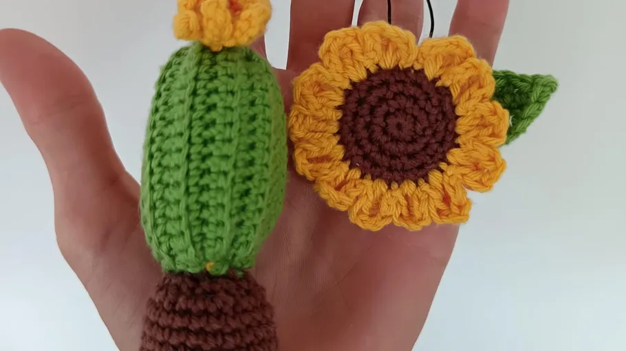 Crocheted cactus and sunflower on a hand.