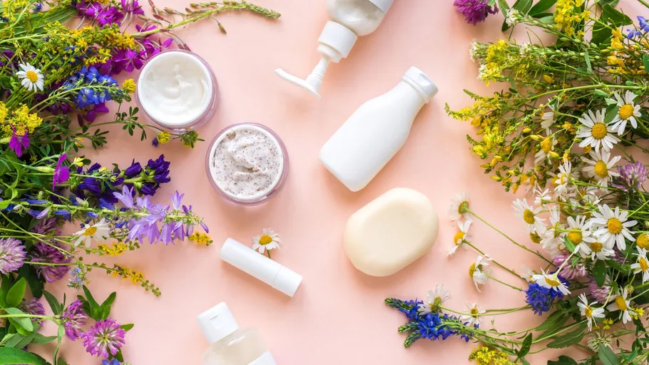 Kosmetikprodukte und Blumen auf rosa Hintergrund.