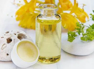 Glass bottle with essential oil, flowers nearby.