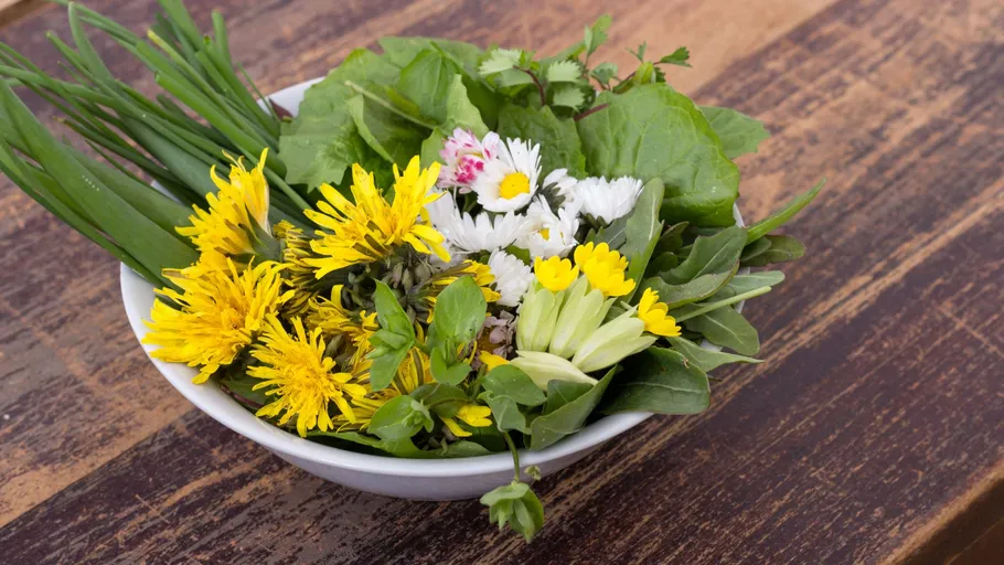 Bowl of fresh edible flowers on table.