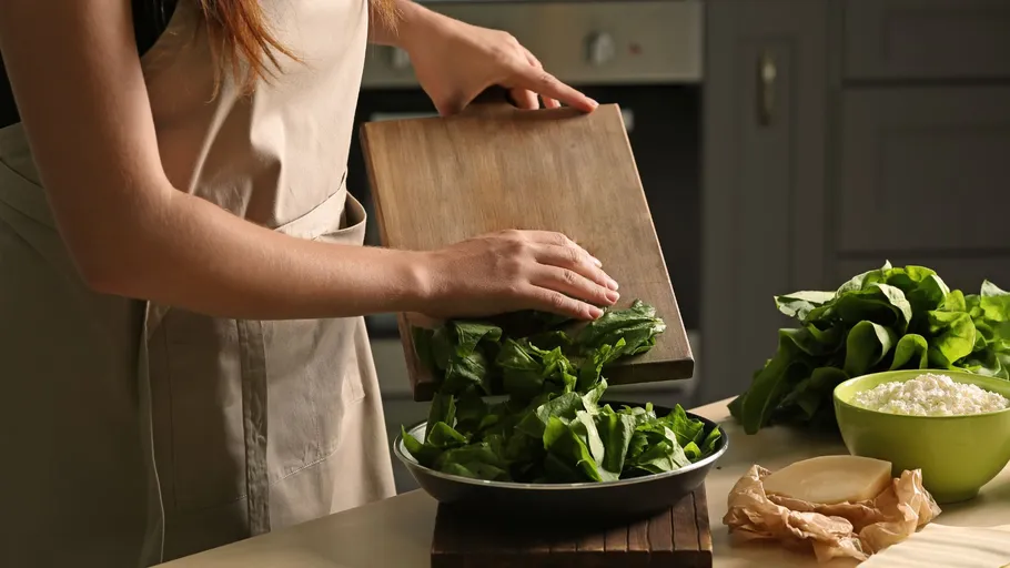 Person placing spinach into a bowl in kitchen.