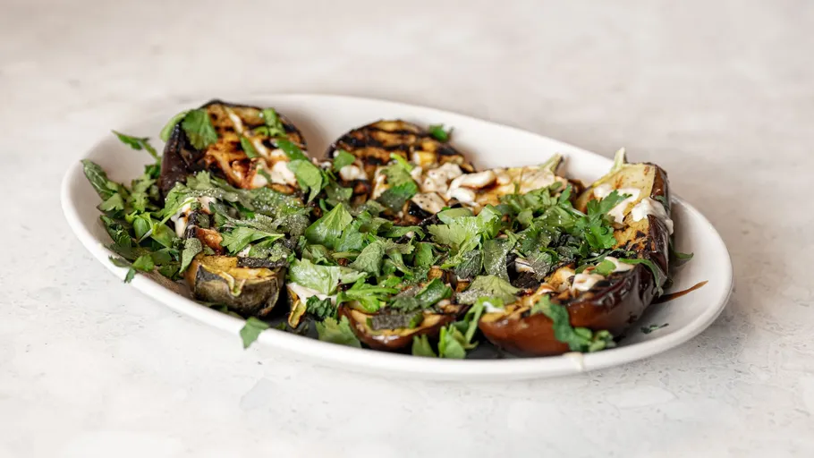 Gegrillte Aubergine mit Kräutern auf weißem Teller.