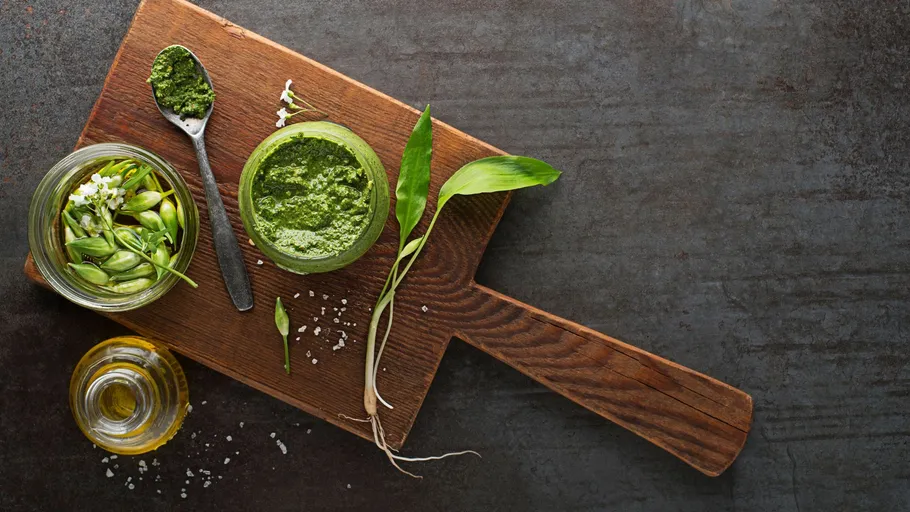 Pesto jar with herbs on wooden board.