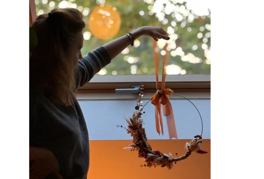 Person hangs decorative wreath in window frame.