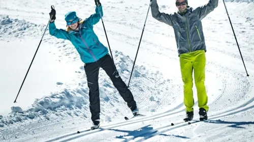Zwei Skifahrer fahren fröhlich auf schneebedecktem Hang.