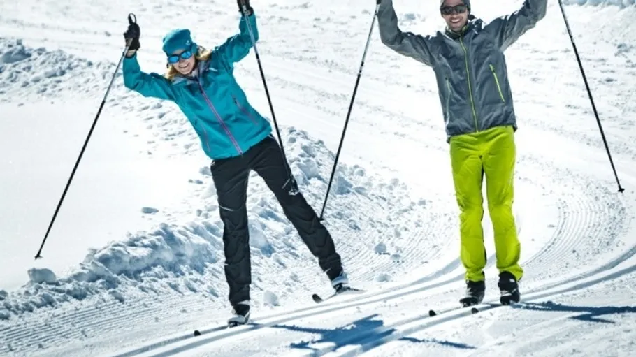 Zwei Skifahrer fahren fröhlich auf schneebedecktem Hang.
