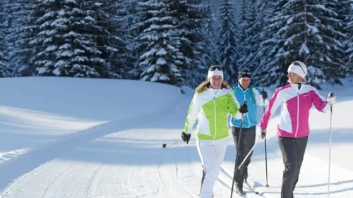 Drei Menschen beim Skifahren auf verschneitem Weg.