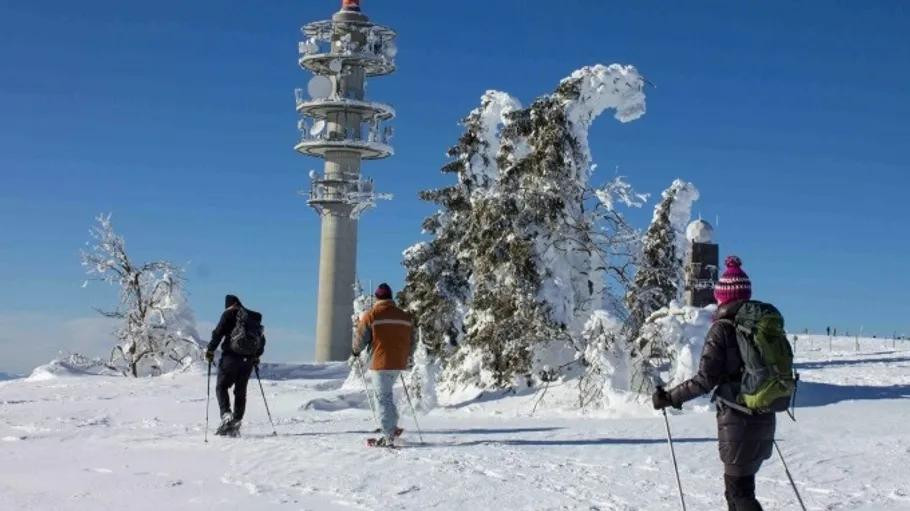 Drei Menschen schneeschuhwandern nahe einem verschneiten Turm.