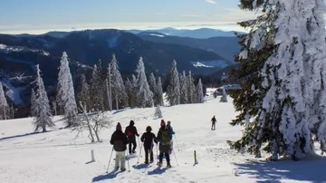 People snowshoe on snowy mountain slope.