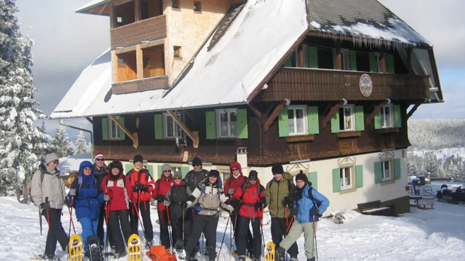 Group poses with snowshoes in front of snowy lodge.