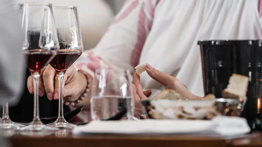 Person holding wine glass and bread at table.