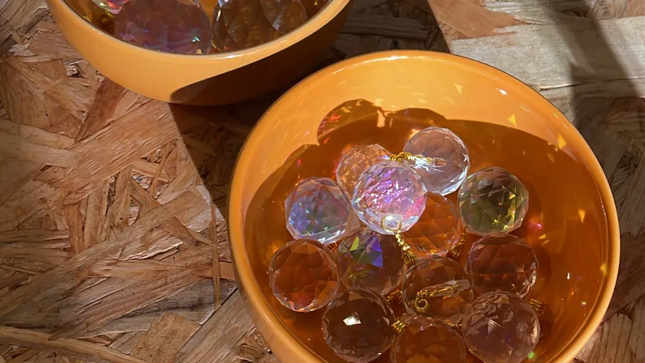 Bunte Kristalle in orangenen Schalen auf Holzoberfläche.