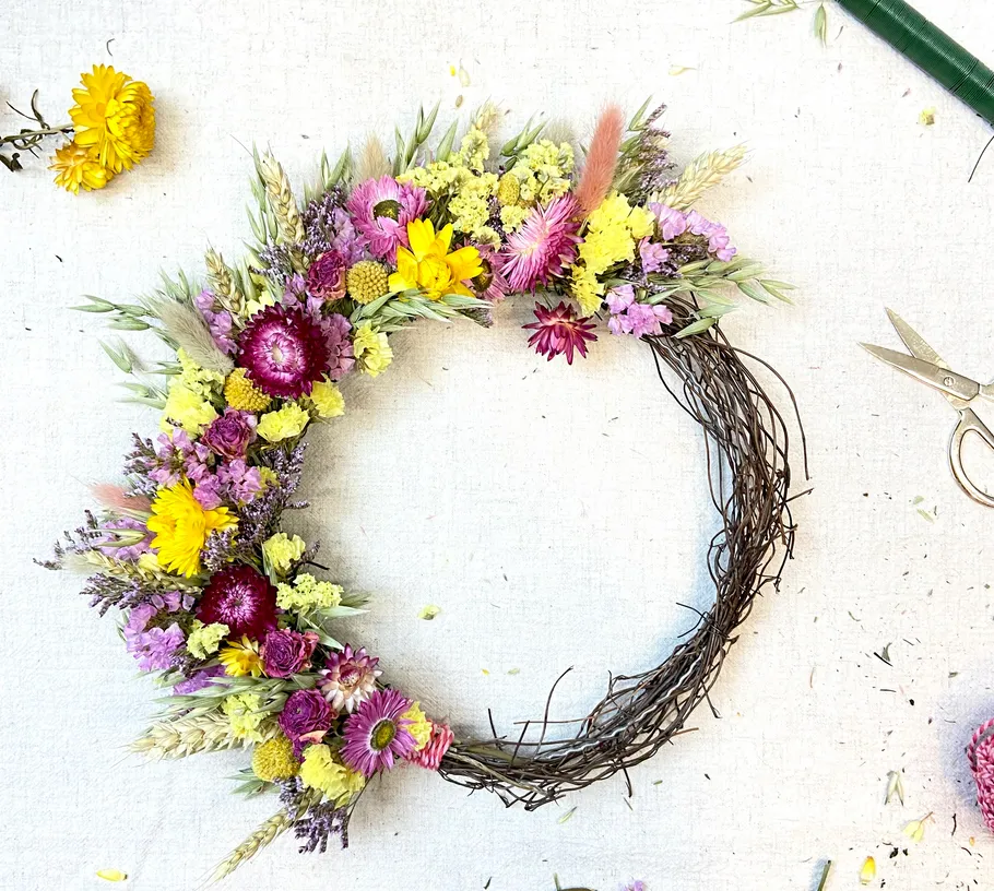 Blumenkranz mit Schere auf weißer Fläche.