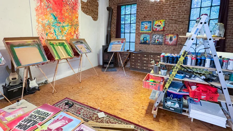 Art studio with paintings and easels, brick walls.