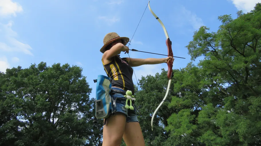 Archer aiming bow outdoors under blue sky.