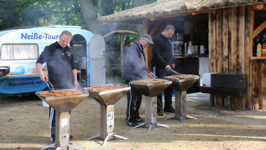 Three men grilling meat near a food stall.