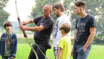 Man teaching archery to group outside.