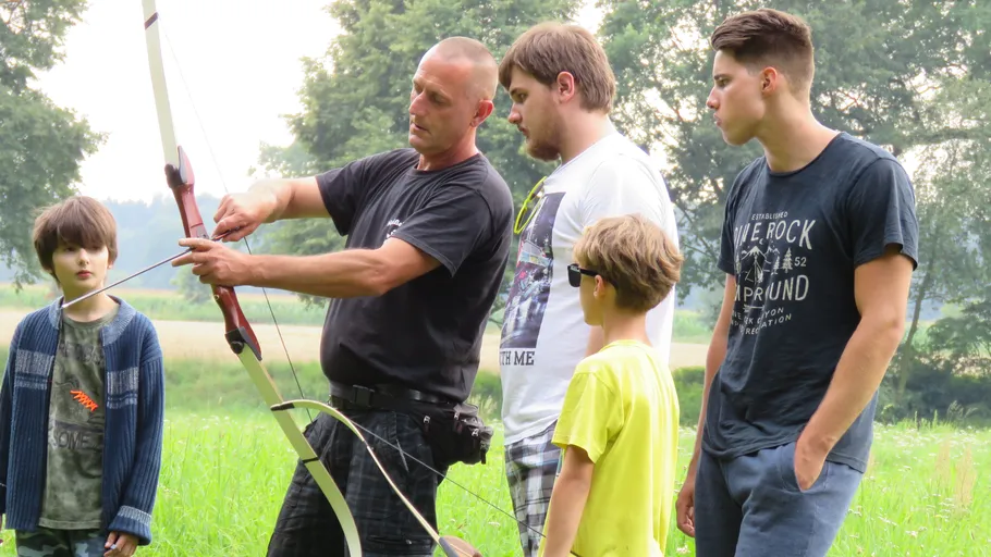 Man teaching archery to group outside.