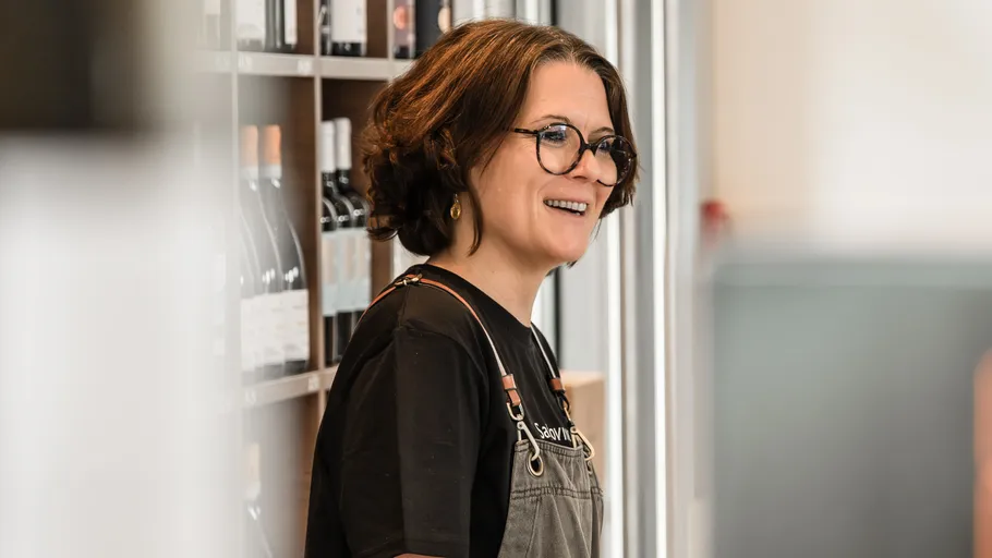 Smiling person in glasses, standing near shelves.