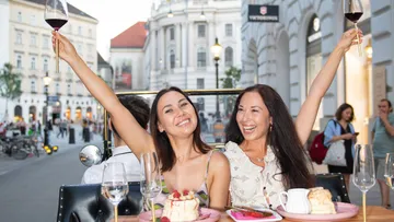 Two women toast with wine glasses outdoors.