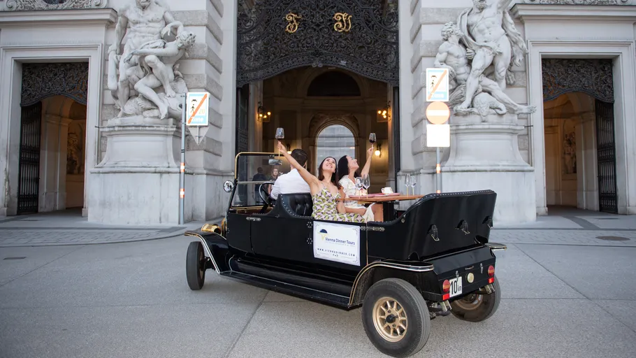 People dining in a vintage car near ornate statues.