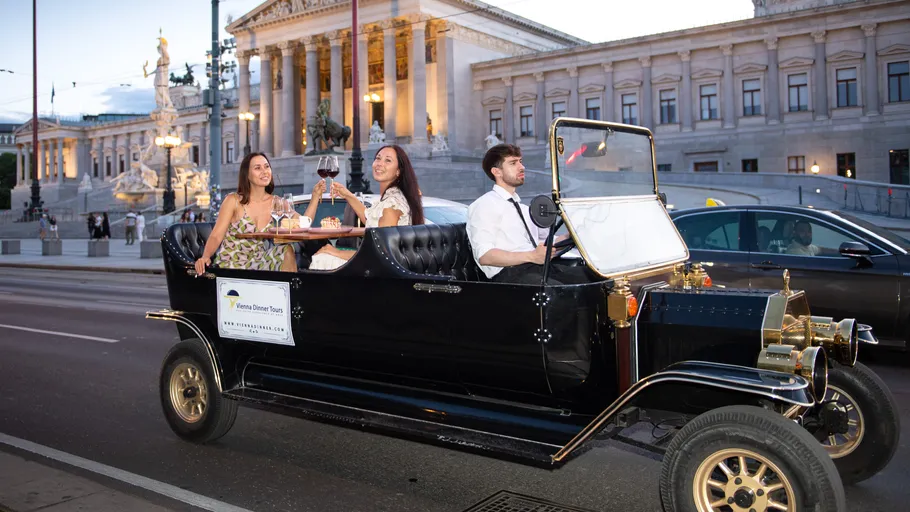 Klassisches Auto mit Passagieren vor großem Gebäude.