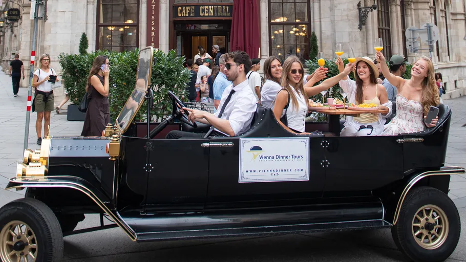 Group celebrates in vintage car outside cafe.