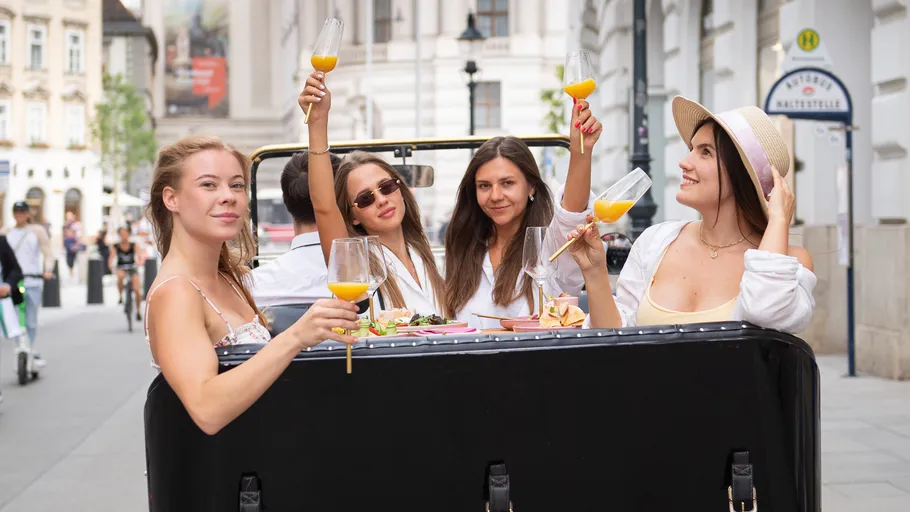 Four women toast in urban street setting.