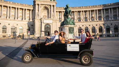 Menschen im Oldtimer vor historischem Gebäude.