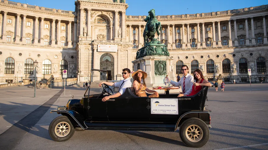 Menschen im Oldtimer vor historischem Gebäude.
