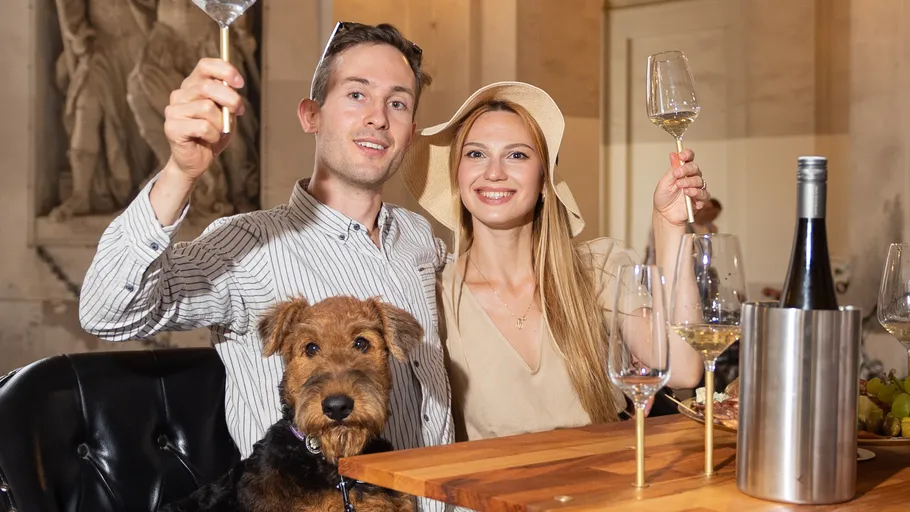 Paar stößt mit Wein an, Hund daneben.