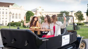 Three women enjoying wine in vintage car.