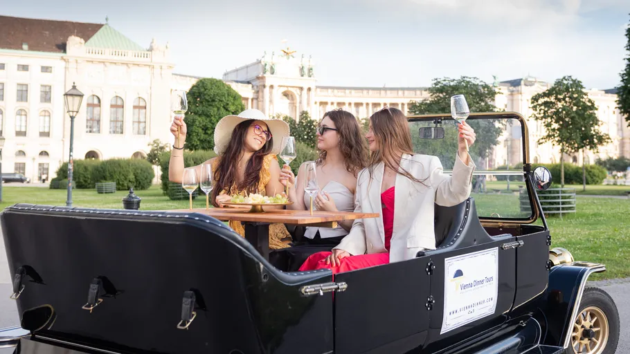 Three women enjoying wine in vintage car.