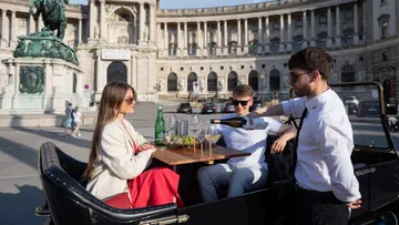 Server pours wine for two seated people outdoors.