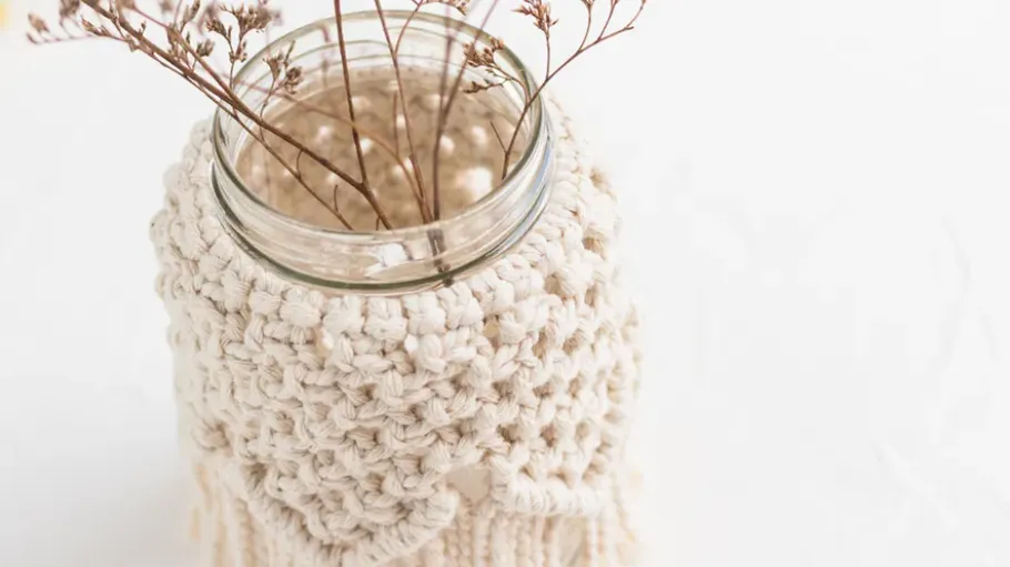 Glass jar with crochet cover and dry twigs.