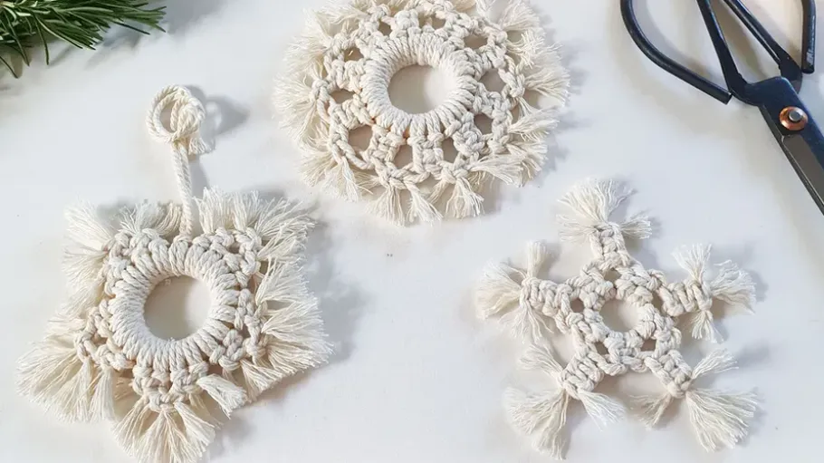 Three macrame snowflakes on a white table.