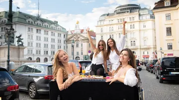 Vier Frauen speisen an Tisch auf Stadtstraße.