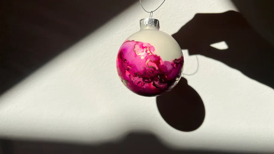 Hand hält pinken Schmuckanhänger vor Wand.
