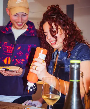 Two people smiling, squeezing sauce in kitchen.