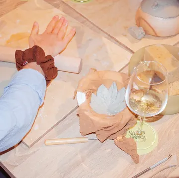 Person shaping clay, wine glass nearby, table surface.