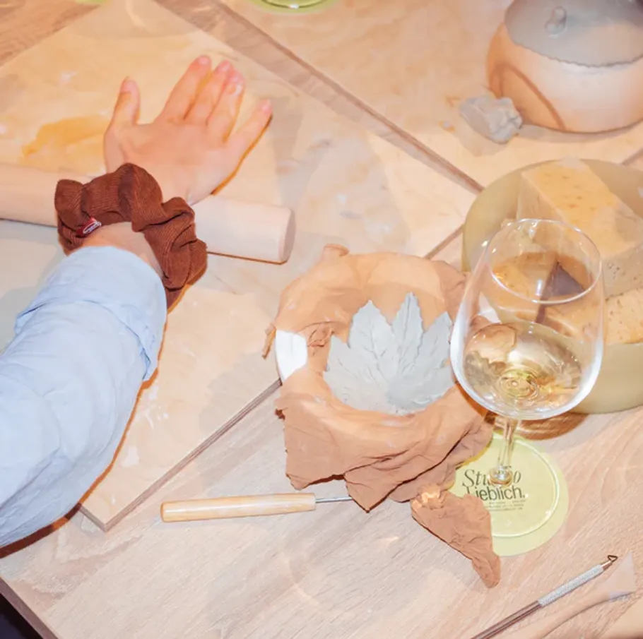 Person shaping clay, wine glass nearby, table surface.