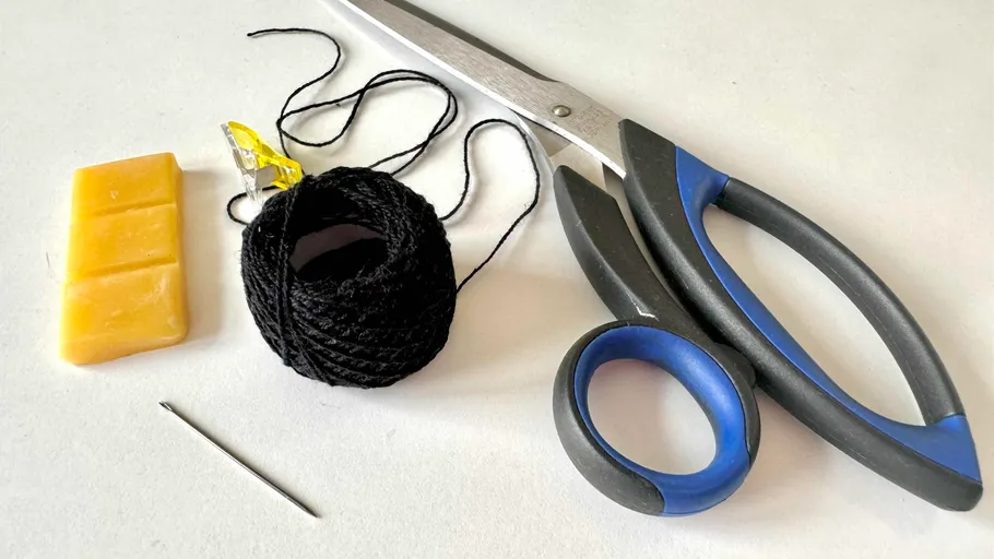 Scissors, thread, needle, and wax on a table.