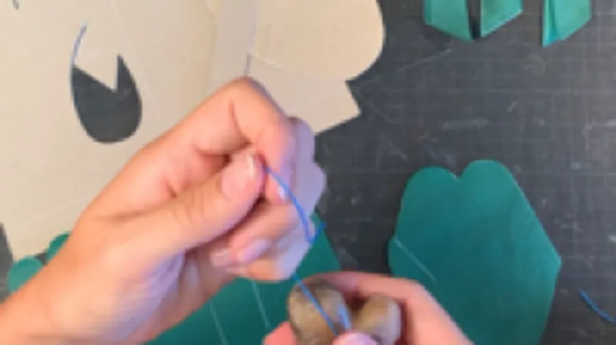 Hands threading blue string through stone.