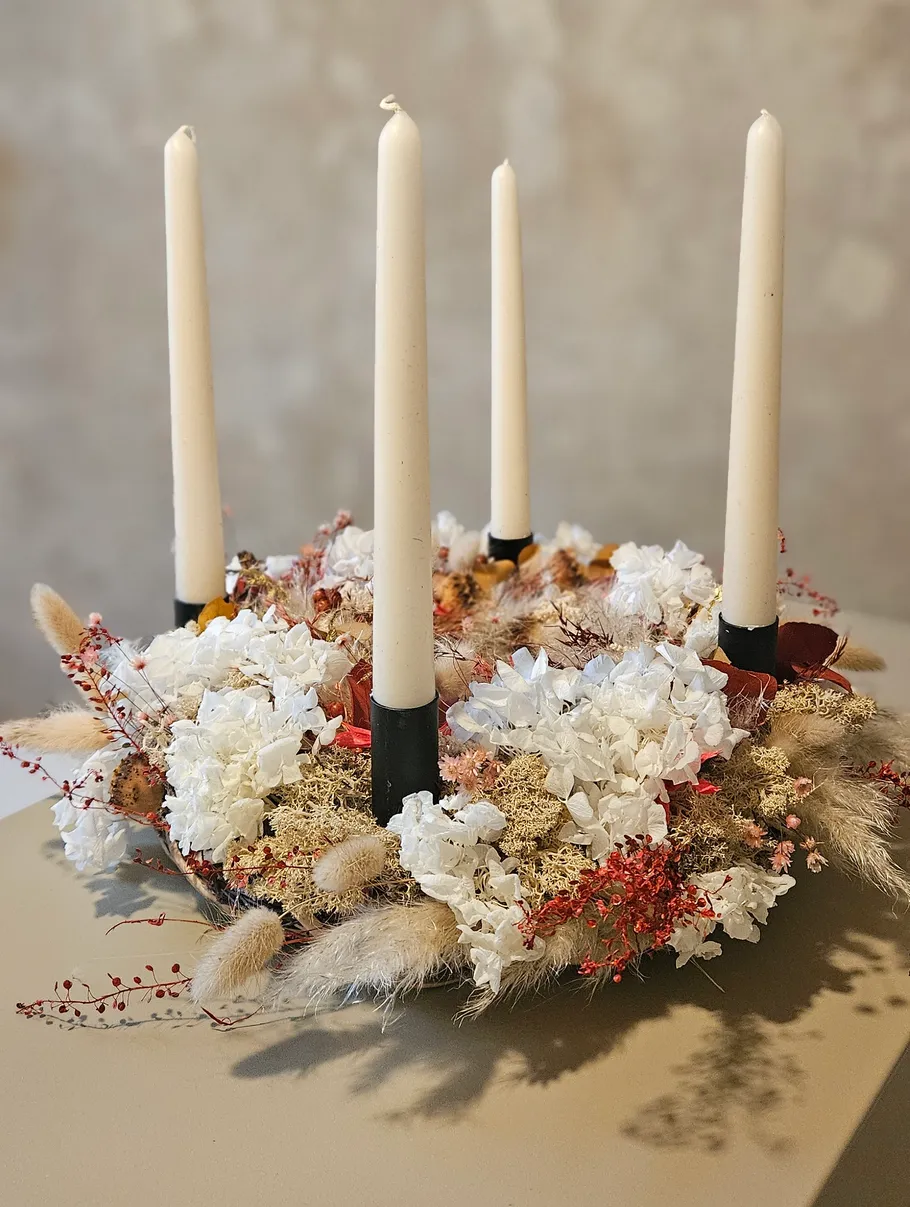 Blumenkranz mit vier hohen Kerzen in der Mitte.